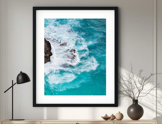 Vertical aerial fine art photography of deep teal ocean waves crashing against a rocky cliff, featuring high-contrast white foam and turquoise gradients.