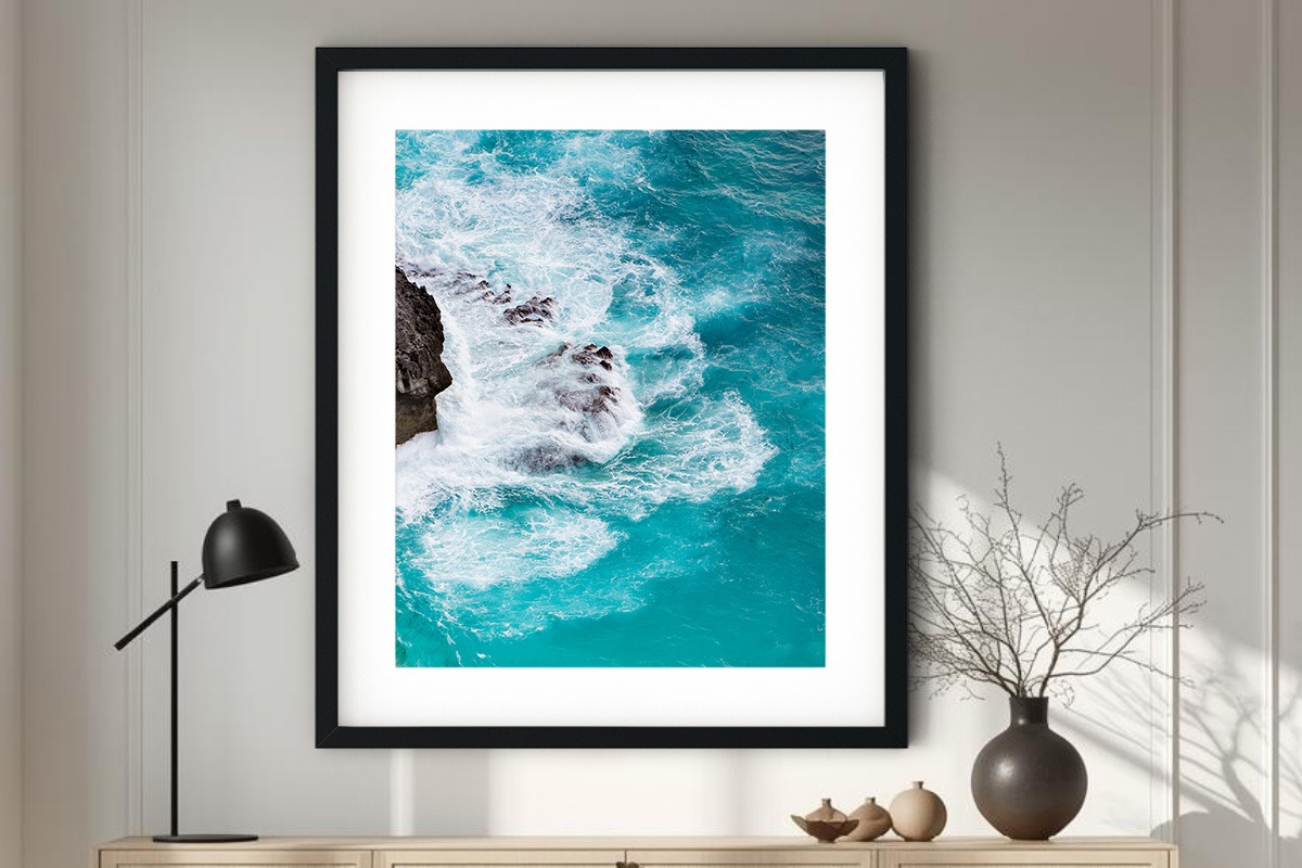 Vertical aerial fine art photography of deep teal ocean waves crashing against a rocky cliff, featuring high-contrast white foam and turquoise gradients.