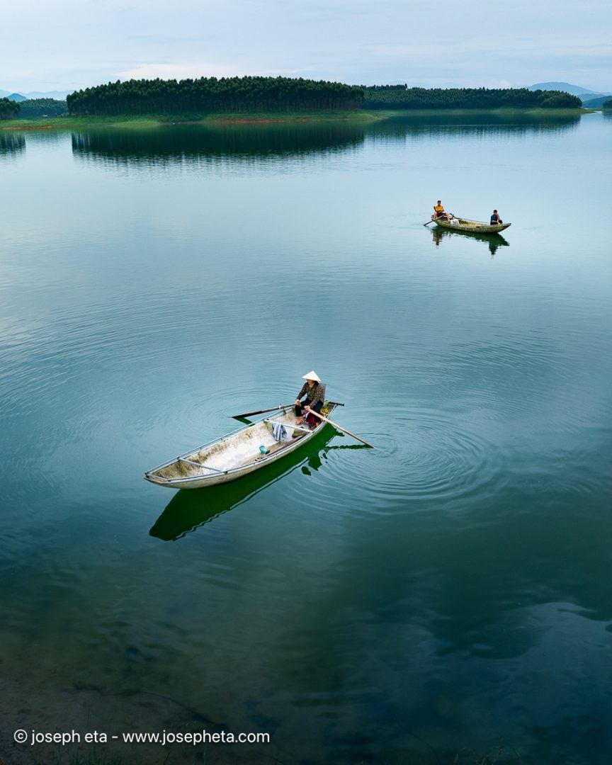 An intimate, low-altitude aerial view that captures the collective rhythm of the fishermen on the water. The consistency of the teal water and the geometric placement of the boats provide visual stability and order, reassuring the viewer.
