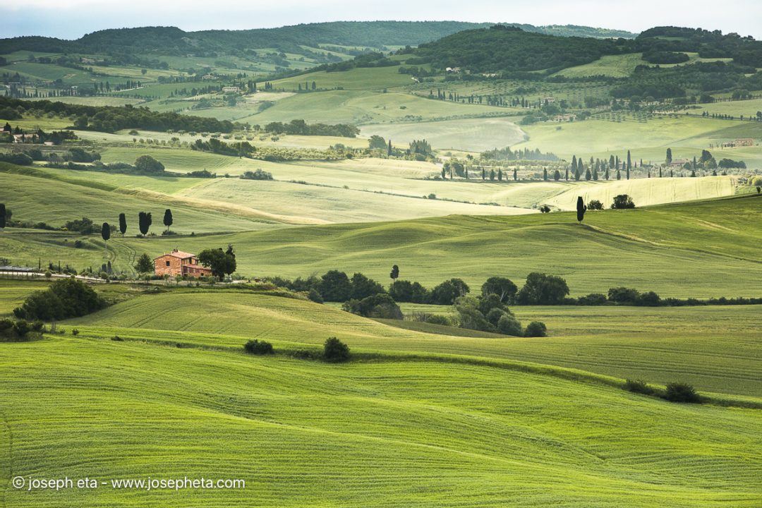 A sweeping green pastoral landscape with a farm house in the Tuscan countryside