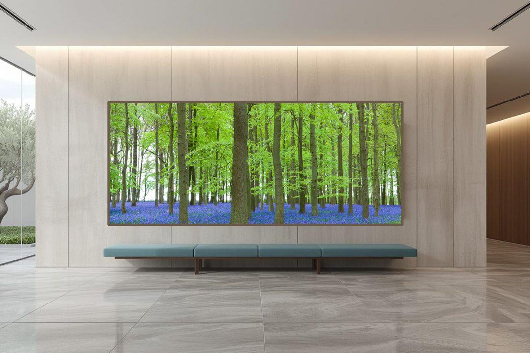 Large panoramic mockup of biophilic fine art photography featuring a dense green forest with a carpet of bluebells, installed in a bright, modern hospital corridor with a blue bench.