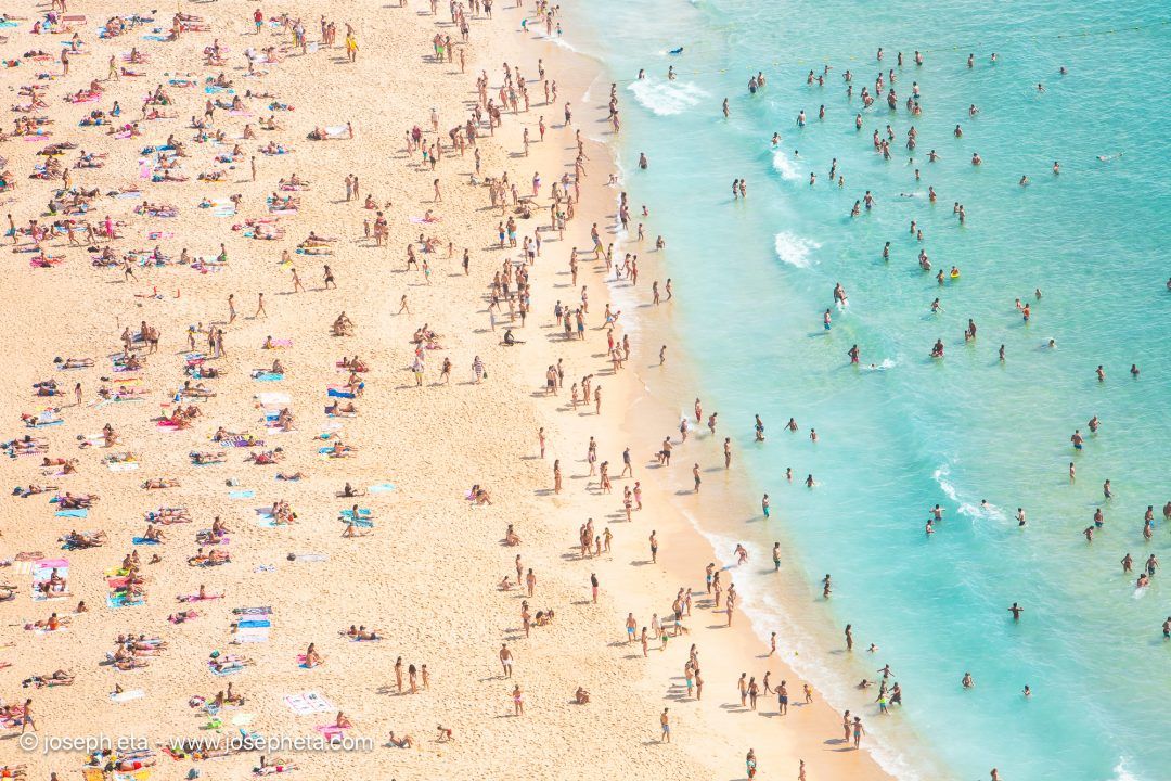 An expansive aerial view where the vibrant primary colors of beach umbrellas pop against warm sand, styled over a light oak sideboard against a warm beige wall to offer cheerful, optimistic energy.