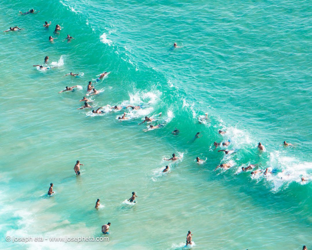 A vibrant, texturally rich top-down aerial view of swimmers cutting through a breaking wave, hung elegantly over a premium white marble floating console table.
