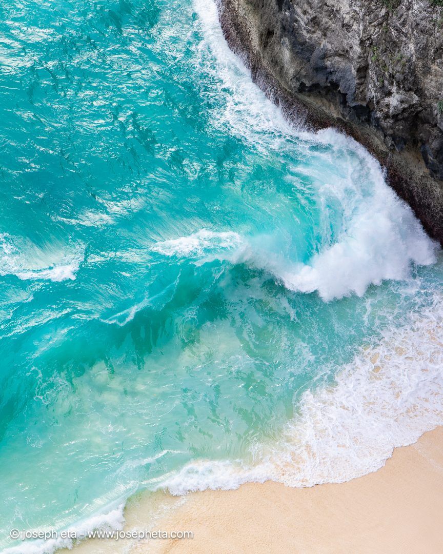 A dramatic, high-contrast aerial shot of deep teal waters meeting raw coastal cliffs, styled over a sleek black contemporary credenza.